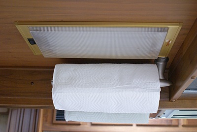 Paper towel holder installed above kitchen sink behind fluorescent light fixture.