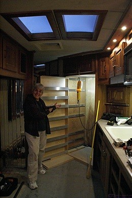 Linda does her Vanna White impersonation, highlighting how the new pull-out pantry will look when it is installed.  The pantry is in its extended position revealing the slides sections that will mount on the cabinet wall.  The refrigerator is out so we can work in the alcove.