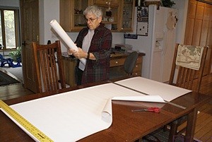 Measuring and cutting wallpaper on the dining room table in the house.
