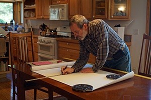 Bruce marks a piece of wallpaper on the dining room table in the house before cutting it.