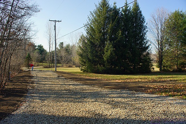 The new gravel driveway extension and RV parking pad. Phil, on the left side of the driveway by the nearer utility pole, rakes out the topsoil he placed along both sides of the driveway.