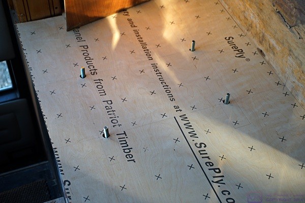 The SurePly underlayment on the co-pilot/navigator platform floor showing how it fits under the outside wall panel and over the four mounting bolts for the seat.